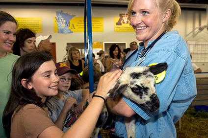 Student holding a goat that is being petted by a young girl at the state fair