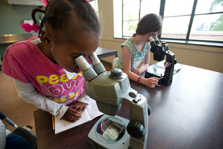 two young children, about 9-10, looking into microscopes in a University lab