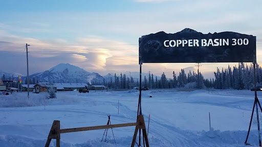 A sign that says "Copper Basin 300" stands in front of a snowy backdrop of mountains and trees