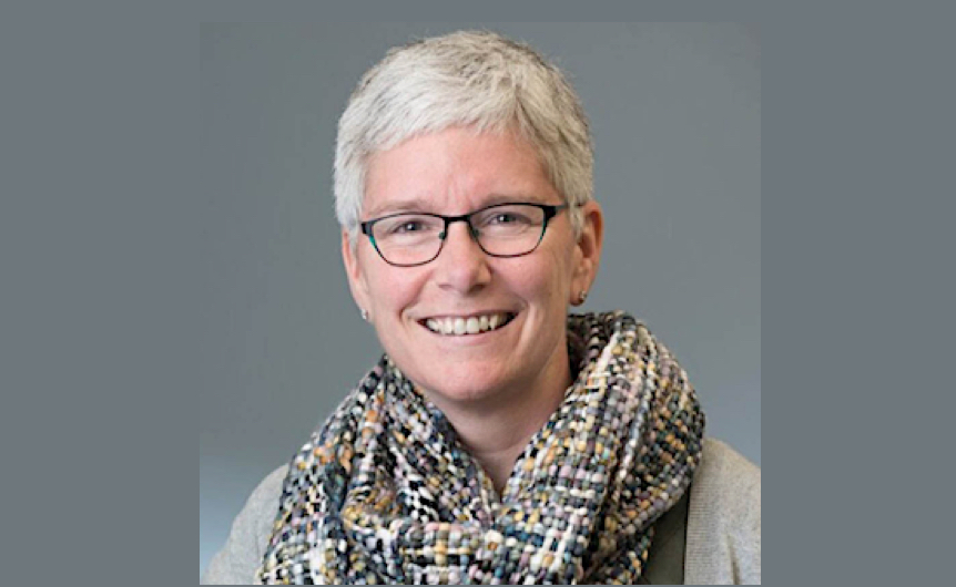 A woman with short white hair and glasses wearing an infinity scarf smiles towards the camera