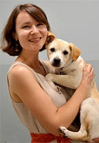A brunette woman stands smiling and holding a puppy