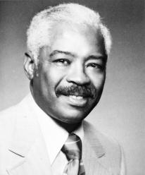A black and white photo of Dr. Iverson Bell wearing a suit smiling at the camera