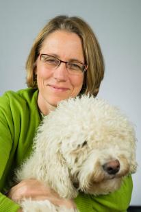 A woman with short brown hair and glasses holding a fluffy white dog