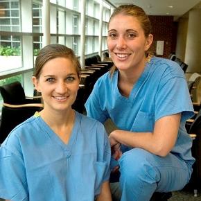 Two students in scrubs sitting in a hallway