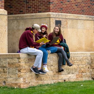 students sit on a wall outside excitedly looking at pamphlets