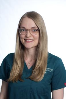 A woman with long blonde hair and glasses wearing a VMC shirt smiles towards the camera