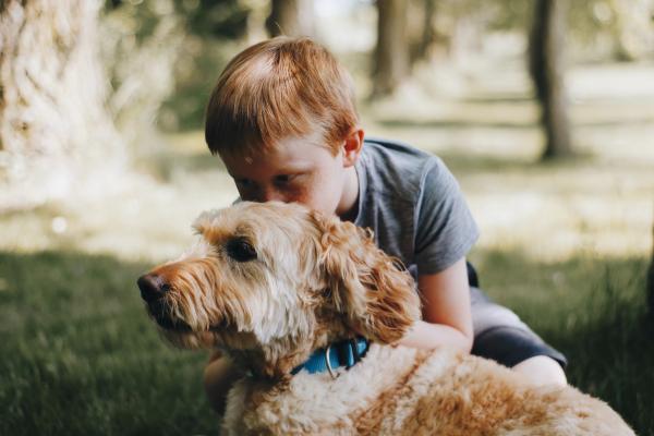 A red headed boy kisses the top of his dog&#039;s head.
