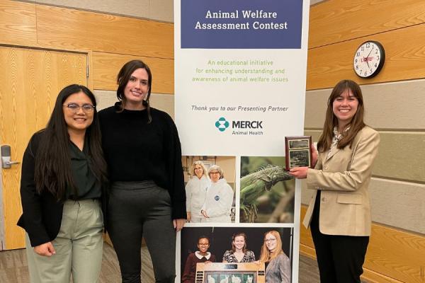 Three women stand around a poster that says &quot;Animal Welfare Assessment Contest&quot;